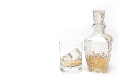 Close up of beautifully decorated crystal glass bottle with whiskey and whiskey glass with ice cubes next to it isolated on white backgroundの写真素材