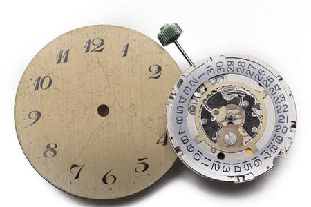 Close up of spare parts from watches a golden dial and a dismantled clockwork with gears on white...