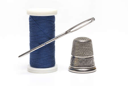 Close up of a blue roll with sewing thread of a sewing needle stuck in it and a silver thimble next...