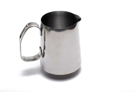 Close up of small metal milk jug with handle for frothing milk foam and milk for making cappuccino and latte art against white backgroundの写真素材