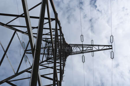 Massive tall high voltage mast pylon photographed sideways from bottom to top with side boom arm high voltage lines and insulators against blue sky with white clouds as concept for power supply and electricityの写真素材