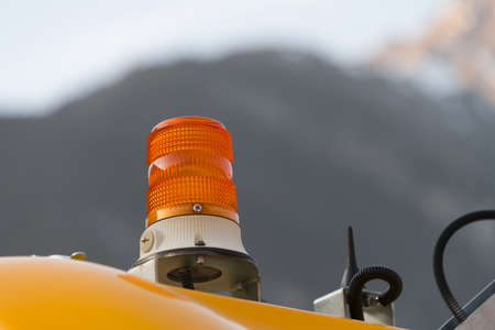 Close up of orange yellow rotating beacon torch lamp as warning light when using work machines and equipment in front of mountains and blue skyの写真素材