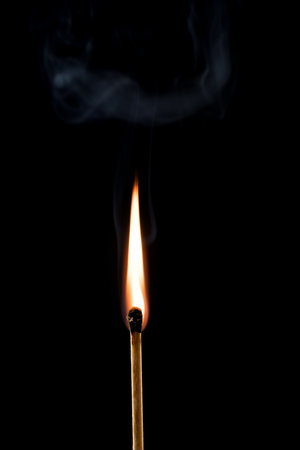 Close up of burning match matchstick shortly after lighting with still visible rising smoke cloud on black background as concept for open fire flames and natural lightの写真素材