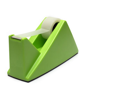 Oblique close up of large solid green heavy tape dispenser as office equipment with transparent plastic strip on white backgroundの写真素材
