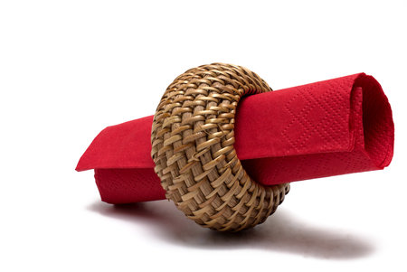 Close up of woven wooden straw serviette ring with rolled red serviette in it on white backgroundの写真素材