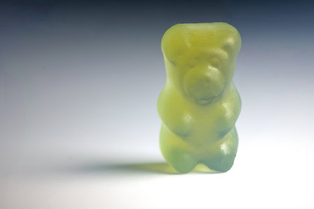 Close up of small green candy gelatin gum jelly figure bear with strong shadow on light backgroundの写真素材