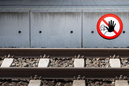 Side of a platform behind a railroad track with clearly visible Stop danger sign with calling face...