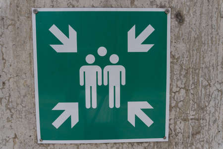 Close up of green sign pointing to a gathering meeting place point mounted on a concrete wall as a...