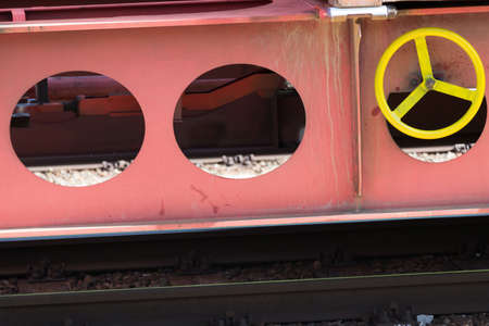 Partial view of the side of a solid steel railroad low loader wagon with visible yellow turning wheel and mechanism for locking the brakes when parked on tracksの写真素材