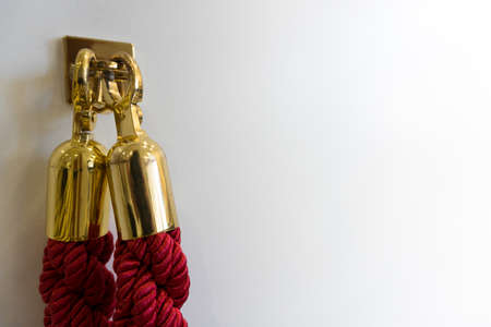 Close up of noble burgundy bordeaux red noble lock chain cord rope with golden ends hooked on a hook against white wall background with copy space as concept for audience entrance at events red carpet and meetingsの写真素材