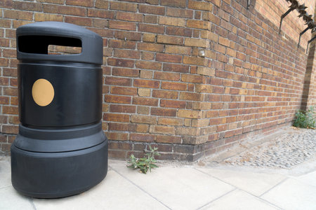 Close up of black modern public trash garbage can on a pavement in London in front of wall corner of brick wall as concept for cleanliness in public and on streetsの写真素材