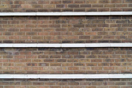 Close up of old facade bricked with fired glazed bricks with three transverse white cornices to use as backgroundの写真素材