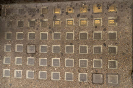 Close up of glass blocks geometrically embedded in partially dirty floor bricks to use as background