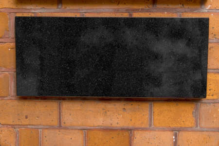 Close up of bricked wall facade laid of glazed fired bricks mounted black marble sign plate offering copy space to use as backgroundの写真素材