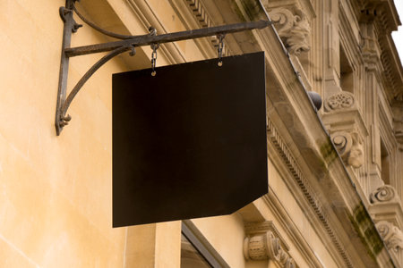 Close-up of an outdoor empty black metal board sign plate offering copy space mounted on old historical facade with antique buildings in the backgroundの写真素材