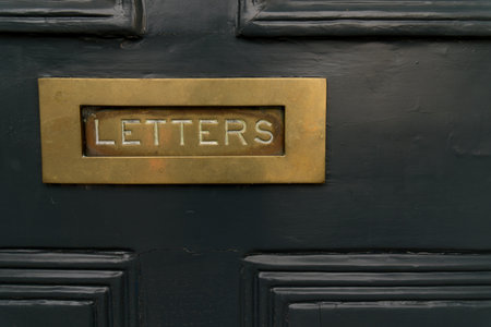 Close up of dark black noble wood entrance door with square mail slot with copper metal brass inscription letters concept for mailings messages and letter deliveryの写真素材