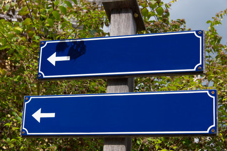 Close up of two blue rustic signposts in front of green trees and bushes with leaves to write on as concept for signs and orientationの写真素材
