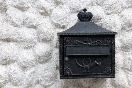 Close up of white rough plastered rustic house facade with black ornate wrought iron mailbox as a concept for postal mail items shipments and transportation of parcelsの写真素材
