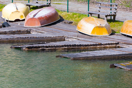 Dilapidated abandoned wooden jetty with upside down colorful old rowboats lying on it at lake as concept for decline of tourism recession and decayの写真素材