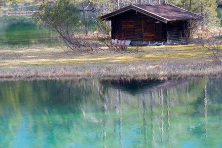 Wooden cottage log cabin at idyllic mountain lake clear reflecting crystal clear water surface in Tyrol as concept emigration living in the wilderness relaxation and living in harmony with natureの写真素材