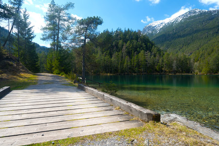 unpaved road with bridge at tyrolean mountain lake under partly cloudy blue sky surrounded by forests as concept living remote places adventure untouched nature expedition wilderness and emigrationの写真素材
