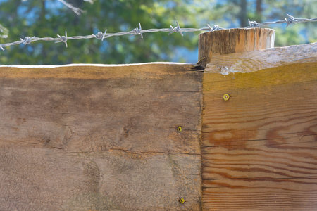 Extreme close up of wooden rustic solid fence barbed stretched above razor wire as a concept cordon enter forbidden being locked up restricted areas and bordersの写真素材