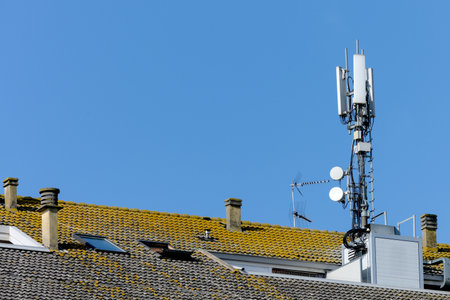 old tiled roof with various fireplaces for solid fuel and a modern large massive 3g 4g 5g mobile internet antenna as a concept for cell phone towers in residential areas and radiation exposureの写真素材