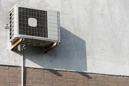 Sunlit house facade wall partially clinker coating with air conditioning mounted outside air conditioning compressor as concept for air conditioning in summer and outdated technologyの写真素材