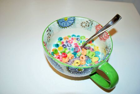 Close up of a bowl full of fruit flavored loops of sugar ready to eat breakfast cereal with a spoon...