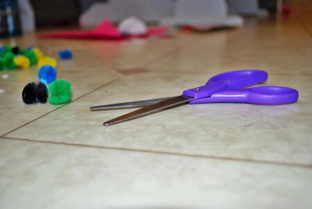 Multi colored cotton balls glue and scissors on a linoleum floor during arts and crafts time