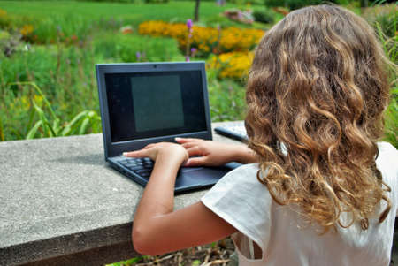 young girl doing school work on a computer remote learning in the park