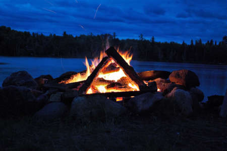 camp fire burning in a fire pit next to the lake