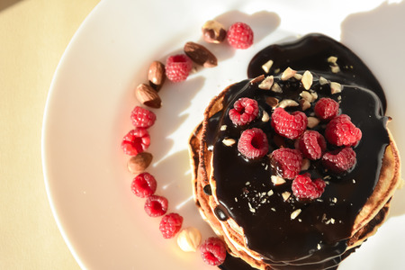 A stack of chocolate pancakes with raspberry and nutsの写真素材