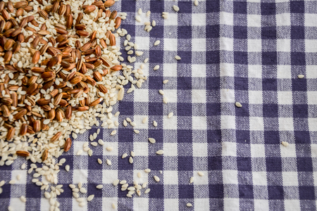 Rice seeds and sesame seeds on a checkered tablecloth. Top viewの写真素材