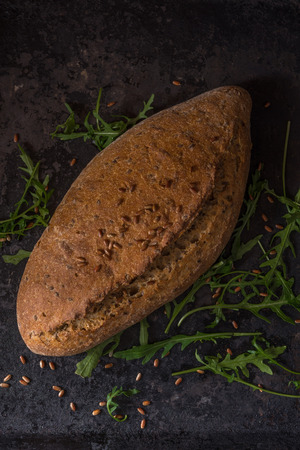 Black food background with homemade bread loaf and fresh aromatic ruccola, copy space. Top viewの写真素材