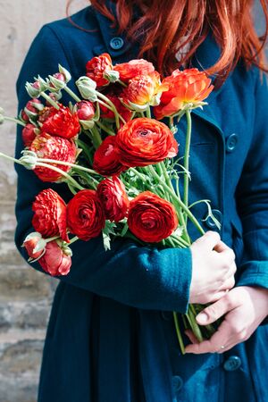 Female hands holding a bouquet of red anunculus  flowers on a rustic background