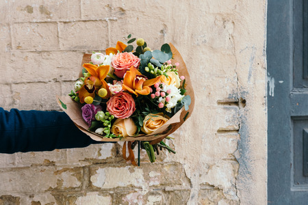 Woman holds colorful bouquet of different fresh flowers against brick wall. Bunch of orchids, roses,...