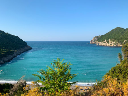 Beach in Greece, mountains in the background. A striking contrast of white walls and green trees, many shades of blue and earth tones under a hazy sky. Walk in nature.の写真素材