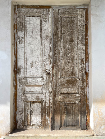 Old weathered antique door as a vintage background. An aged dull muted brown of cracked, peeling paint, exposed greyish wood underneath. Entrance to an old house in Greece.の写真素材