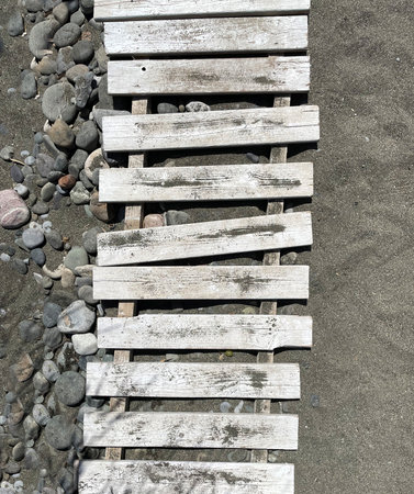 Wooden path on rocks and sand as background. Rustic beach path with wooden planks on two crossbars,laying in golden sand. Close up. Wooden floor for protectionの写真素材