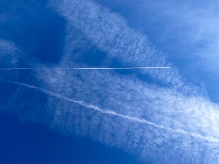 Light white clouds as a background. Blue color of the summer sky, thinned by transparent haze. Cloud layers and a trail of a flying airplane in Greece. Calm carefree feeling.の写真素材