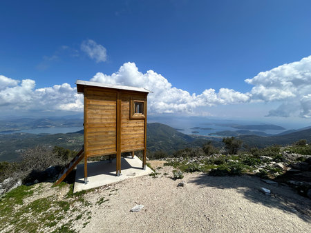 A small observation booth stands on the side of a mountain, offering a stunning view of the hills, the sea and scattered islands. The sky is bright, cloudy, and nature stretchesの写真素材