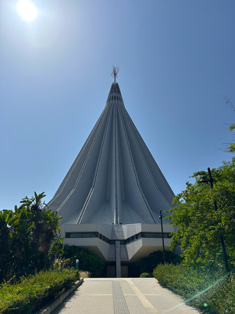 A modern conical church rises tall under the bright sun, surrounded by lush green trees. This is the Sanctuary of Our Lady of Tears in Syracuse, Sicily,の写真素材