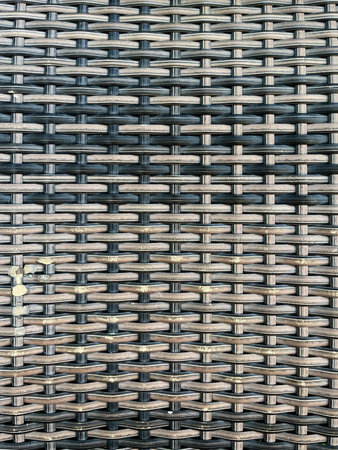 This close-up image shows a tightly woven rattan or synthetic wicker pattern in shades of brown and...
