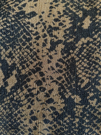 a close-up of a fabric with a reptile or snakeskin-inspired pattern. The texture is detailed, with...