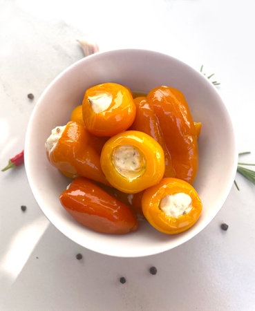 Stuffed orange cherry peppers and bell peppers with creamy cheese filling in white bowl. Gourmet...