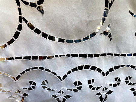 White fabric with decorative cutwork embroidery, featuring ornamental swirls and geometric patterns....