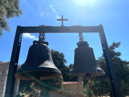 Two old bronze church bells with engraved religious figures, hanging on chains against a blue sky...