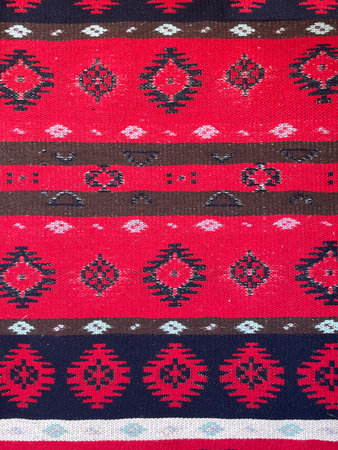 Traditional ethnic textile pattern with geometric ornaments in red, black, and brown colors. Woven...