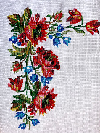 Colorful floral cross-stitch embroidery on white fabric, featuring red poppies and blue bell flowers with green leaves. Traditional handmade needlework design ideal for craftsの写真素材